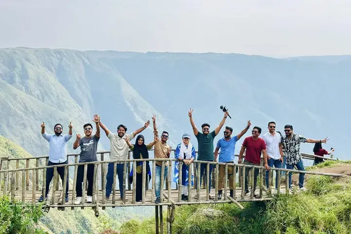 The team with arms raised on a cliff viewpoint above a Meghalaya valley